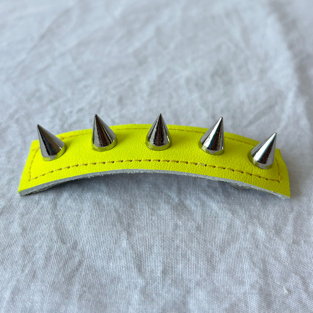 Neon yellow leather barrette with silver spikes on a gray fabric background