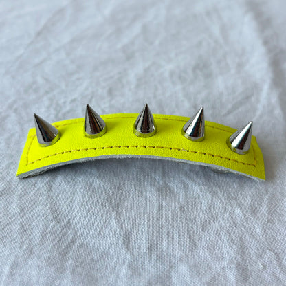 Neon yellow leather barrette with silver spikes on a gray fabric background