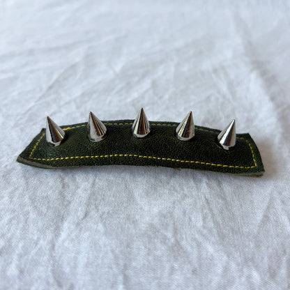 Green leather barrette with silver spikes on a white fabric background