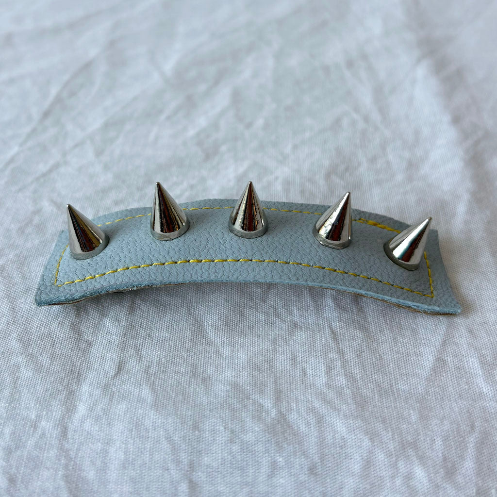 Leather barrette with five metal spikes on a textured gray background