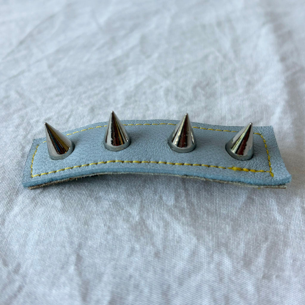 Blue leather barrette with four metal spikes on a white fabric background