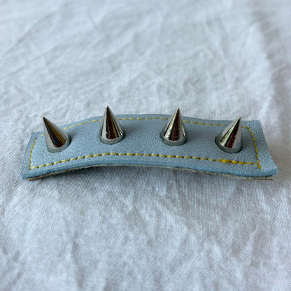 Blue leather barrette with four metal spikes on a white fabric background