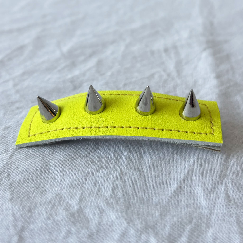 Neon yellow leather barrette with silver spikes on a gray background