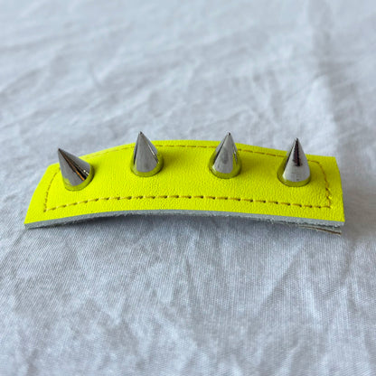 Neon yellow leather barrette with silver spikes on a gray background