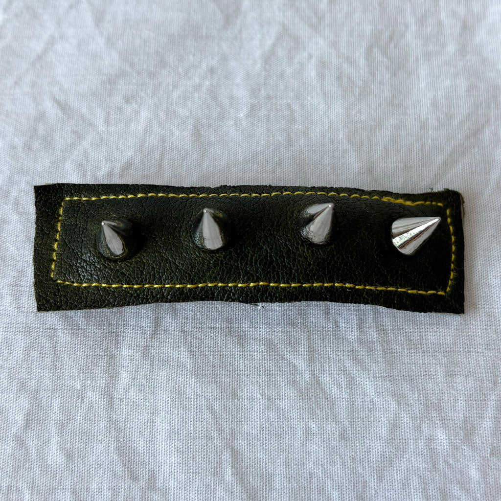 Black leather barrette with silver studs on a gray fabric background